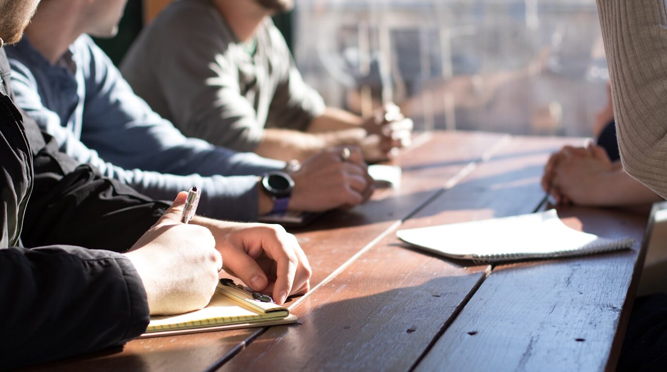 Hands taking notes around a boardroom table during a review discussion.