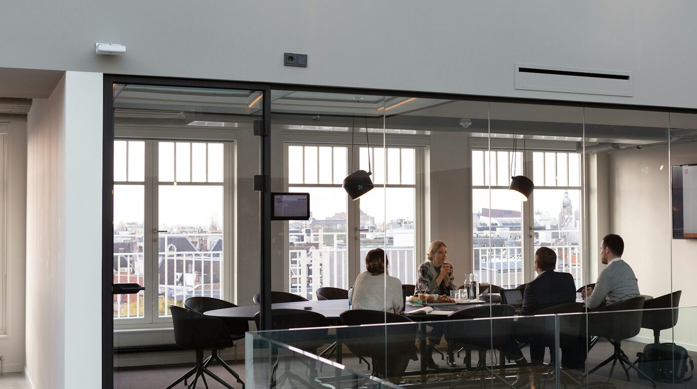 A meeting under way in a glass-walled boardroom, visible from the corridor outside.